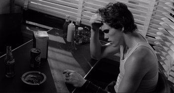 Movie still from “Rumble Fish” (1983), directed by Francis Ford Coppola – A man sitting at a table with a cigarette in his hand; Medium shot, Over the shoulder angle