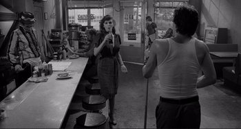 Movie still from “Rumble Fish” (1983), directed by Francis Ford Coppola – A woman standing in front of a counter in a restaurant; Medium shot, Over the shoulder angle