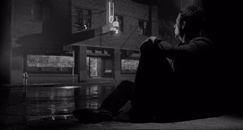 Movie still from “Rumble Fish” (1983), directed by Francis Ford Coppola – A man sitting on the ground in front of a street light; Wide shot, Low angle