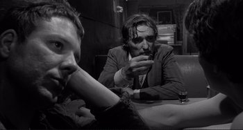 Movie still from “Rumble Fish” (1983), directed by Francis Ford Coppola – A man smoking a cigarette while another man sits at a table; Close Up shot, Over the shoulder angle