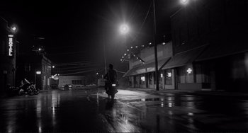 Movie still from “Rumble Fish” (1983), directed by Francis Ford Coppola – A man riding a motorcycle down a street at night; Extreme Wide shot, Low angle