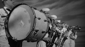 Movie still from “Run Silent Run Deep” (1958), directed by Robert Wise – A group of men playing musical instruments in front of a cloudy sky; Medium shot, Low angle