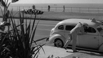 Movie still from “Run Silent Run Deep” (1958), directed by Robert Wise – An old car parked on the side of the road near the ocean; Wide shot, High angle