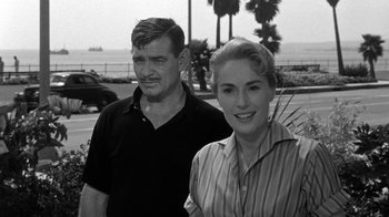 Movie still from “Run Silent Run Deep” (1958), directed by Robert Wise – An older man standing next to an older woman in front of palm trees; Medium shot, Over the shoulder angle