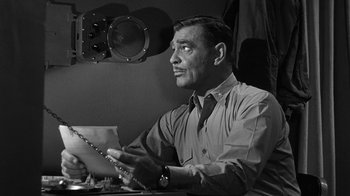 Movie still from “Run Silent Run Deep” (1958), directed by Robert Wise – A man sitting at a table holding a piece of paper; Close Up shot, Low angle