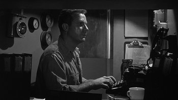 Movie still from “Run Silent Run Deep” (1958), directed by Robert Wise – A black and white photo of a man typing on a typewriter; Medium shot, Low angle