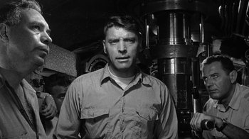Movie still from “Run Silent Run Deep” (1958), directed by Robert Wise – Black and white photograph of a man in front of a machine; Medium shot, Low angle
