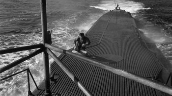Movie still from “Run Silent Run Deep” (1958), directed by Robert Wise – A man standing on the deck of a boat in the ocean; Wide shot, High angle