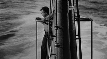 Movie still from “Run Silent Run Deep” (1958), directed by Robert Wise – A black and white photo of a man standing on a pier; Medium shot, High angle