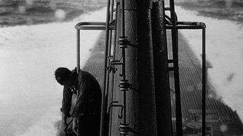 Movie still from “Run Silent Run Deep” (1958), directed by Robert Wise – A man standing next to a metal pole on top of a building; Wide shot, High angle