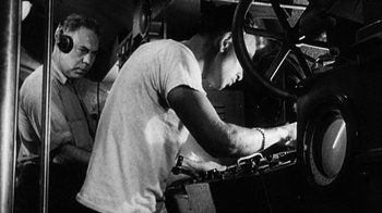 Movie still from “Run Silent Run Deep” (1958), directed by Robert Wise – A man working on a machine in a factory; Medium shot, Low angle