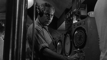 Movie still from “Run Silent Run Deep” (1958), directed by Robert Wise – An older man wearing headphones in front of a radio; Medium shot, Low angle