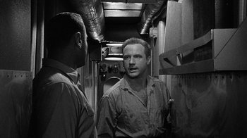 Movie still from “Run Silent Run Deep” (1958), directed by Robert Wise – Two men are standing in a room talking to each other; Medium shot, Over the shoulder angle