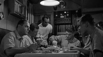 Movie still from “Run Silent Run Deep” (1958), directed by Robert Wise – A black and white photo of a group of men sitting at a table; Medium shot, High angle