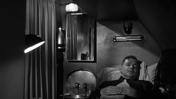 Movie still from “Run Silent Run Deep” (1958), directed by Robert Wise – A black and white photo of a man laying in bed; Medium shot, High angle