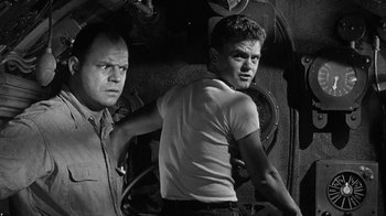 Movie still from “Run Silent Run Deep” (1958), directed by Robert Wise – Two men standing next to each other in front of an engine; Medium shot, Low angle