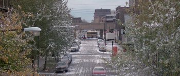 Movie still from “Running Scared” (1986), directed by Peter Hyams – A city street filled with snow and cars parked on the side of the road; Extreme Wide shot, High angle