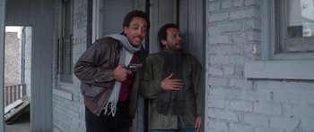 Movie still from “Running Scared” (1986), directed by Peter Hyams – Two men standing next to each other and one is holding a gun; Medium shot, Low angle