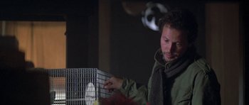 A man in a green jacket holding a bird cage