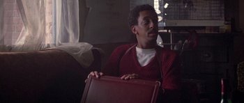 Movie still from “Running Scared” (1986), directed by Peter Hyams – A man holding a brown briefcase in a room; Close Up shot, Over the shoulder angle