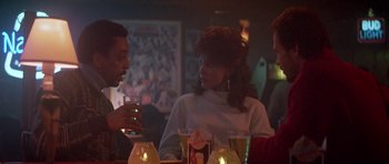 Movie still from “Running Scared” (1986), directed by Peter Hyams – A man and a woman sitting at a table with drinks in front of them; Medium shot, Over the shoulder angle
