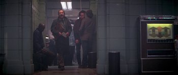 Movie still from “Running Scared” (1986), directed by Peter Hyams – A group of people standing in a room; Wide shot, Over the shoulder angle