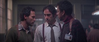 Movie still from “Running Scared” (1986), directed by Peter Hyams – A group of men standing next to each other in a room; Close Up shot, Over the shoulder angle