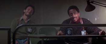 Movie still from “Running Scared” (1986), directed by Peter Hyams – Two men sitting at a table in front of each other; Medium shot, Over the shoulder angle