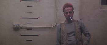 Movie still from “Running Scared” (1986), directed by Peter Hyams – A man smoking a cigarette in front of a scale; Medium shot, Low angle