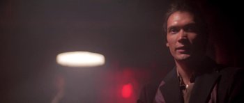 Movie still from “Running Scared” (1986), directed by Peter Hyams – A man standing next to a light in a dark room; Close Up shot, Low angle