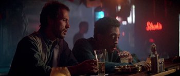 Movie still from “Running Scared” (1986), directed by Peter Hyams – A couple of men sitting at a dinner table; Medium shot, Low angle