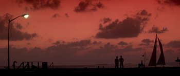 Movie still from “Running Scared” (1986), directed by Peter Hyams – Two people standing on the beach watching the sunset; Extreme Wide shot, Low angle