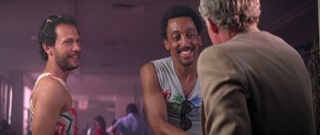 Movie still from “Running Scared” (1986), directed by Peter Hyams – A man smiling at another man at a party; Close Up shot, Low angle