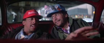 Movie still from “Running Scared” (1986), directed by Peter Hyams – Two men sitting in the back of a car wearing hats; Close Up shot, Low angle