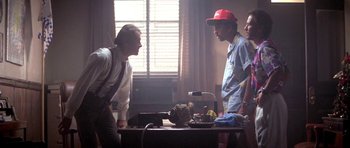 Movie still from “Running Scared” (1986), directed by Peter Hyams – Two men are standing at a table talking to each other; Medium shot, Low angle