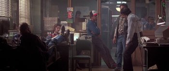 Movie still from “Running Scared” (1986), directed by Peter Hyams – A group of people sitting in a room; Wide shot, Low angle