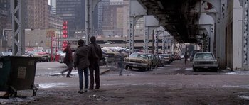 Movie still from “Running Scared” (1986), directed by Peter Hyams – Two people standing on the side of a road; Wide shot, High angle