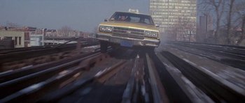 Movie still from “Running Scared” (1986), directed by Peter Hyams – A yellow taxi cab driving down a train track; Wide shot, Low angle