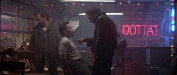 Movie still from “Running Scared” (1986), directed by Peter Hyams – Two men are talking in a room with lights; Medium shot, Over the shoulder angle