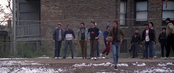 Movie still from “Running Scared” (1986), directed by Peter Hyams – A group of young men standing on top of a dirt field; Wide shot, Low angle