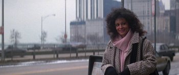 Movie still from “Running Scared” (1986), directed by Peter Hyams – A woman sitting on a bench in the street; Medium shot, Over the shoulder angle