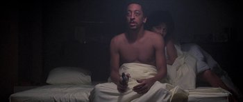 Movie still from “Running Scared” (1986), directed by Peter Hyams – A man sitting on a bed holding a nintendo wii controller; Medium shot, Low angle