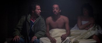 Movie still from “Running Scared” (1986), directed by Peter Hyams – A man sitting next to another man on a bed; Medium shot, Low angle