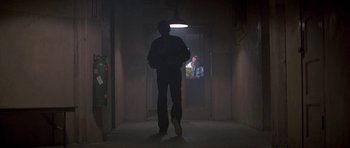 Movie still from “Running Scared” (1986), directed by Peter Hyams – A man standing in a dark room with a light on; Wide shot, Low angle