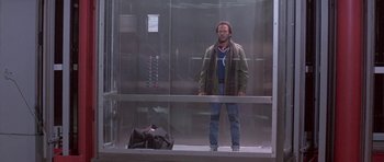 Movie still from “Running Scared” (1986), directed by Peter Hyams – A man standing next to an elevator with a bag; Wide shot, Low angle