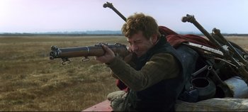 Movie still from “Ryan's Daughter” (1970), directed by David Lean – A man holding a rifle in a field; Medium shot, Over the shoulder angle
