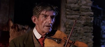 An older man holding a violin while wearing a red tie