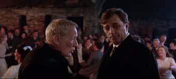 Movie still from “Ryan's Daughter” (1970), directed by David Lean – Two men in suits talking to each other in front of a crowd of onlookers; Close Up shot, Over the shoulder angle