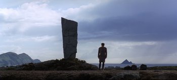 Movie still from “Ryan's Daughter” (1970), directed by David Lean – A man standing in front of a stone sculpture; Wide shot, Low angle