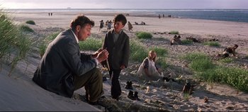 Movie still from “Ryan's Daughter” (1970), directed by David Lean – A man kneeling down on the beach next to two children; Wide shot, Over the shoulder angle